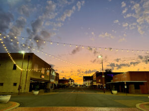 String lights glow above Broad Street in downtown Texarkana, Arkansas, at sunset, casting a warm ambiance over historic brick buildings and creating a picturesque view of the city’s lively entertainment district.