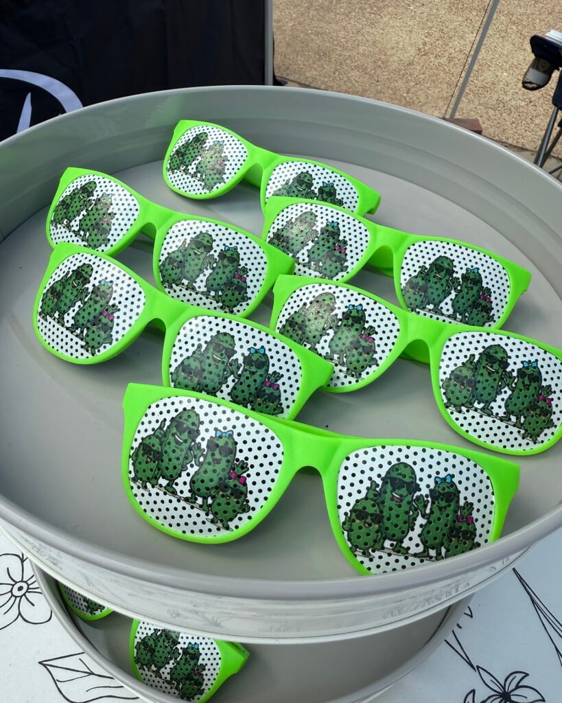 Bright green sunglasses decorated with cartoon pickle characters on display at Texarkana Pickle Fest 2025 in Texarkana, Arkansas.