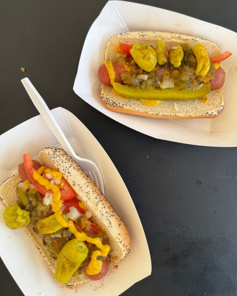 Two loaded hot dogs topped with pickles, peppers, onions, and mustard served in paper trays at Texarkana Pickle Fest 2025 in Texarkana, Arkansas.