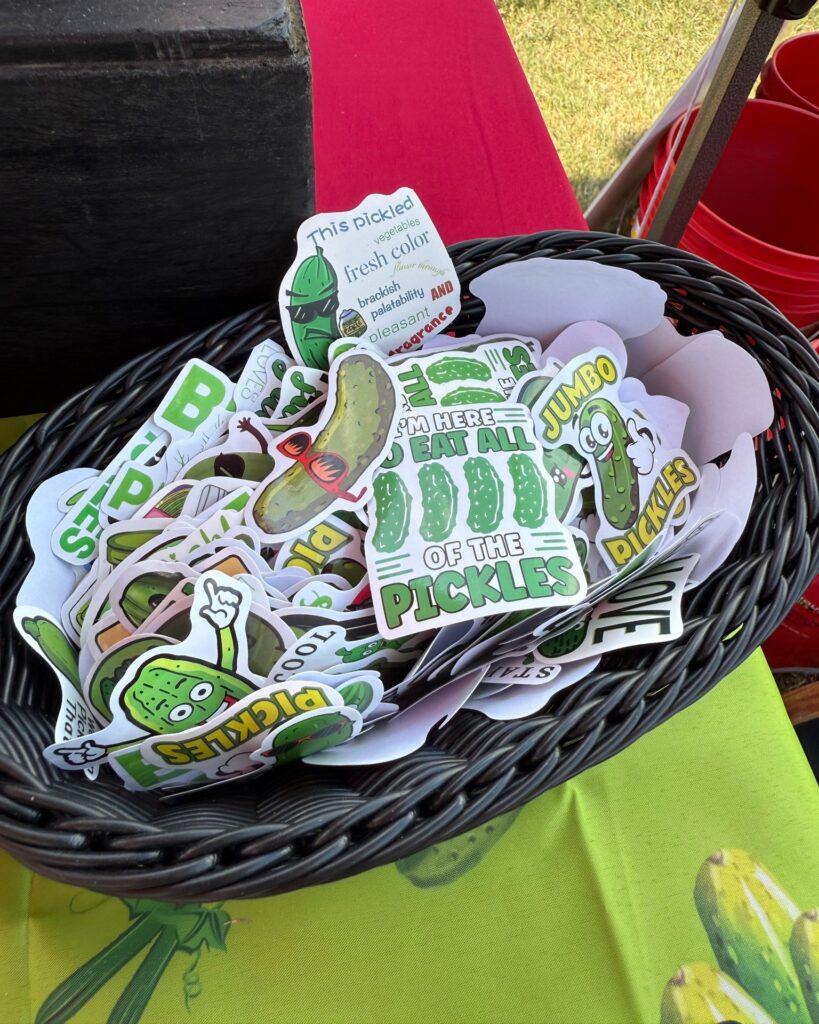 Basket of quirky pickle-themed stickers with playful sayings like “I’m here to eat all the pickles” at Texarkana Pickle Fest 2025 in Texarkana, Arkansas.