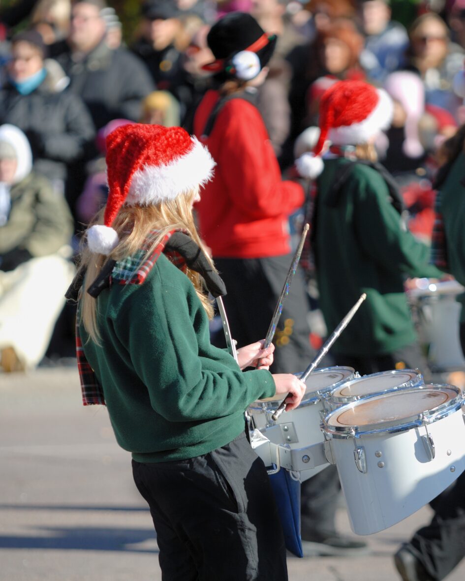 Marching band members wearing Santa hats play drums during a festive Christmas parade.