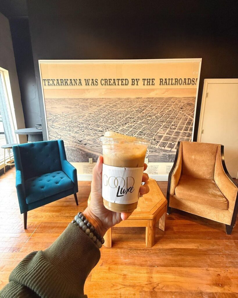 Hand holding an iced coffee from Good Luxe inside a Texarkana café.