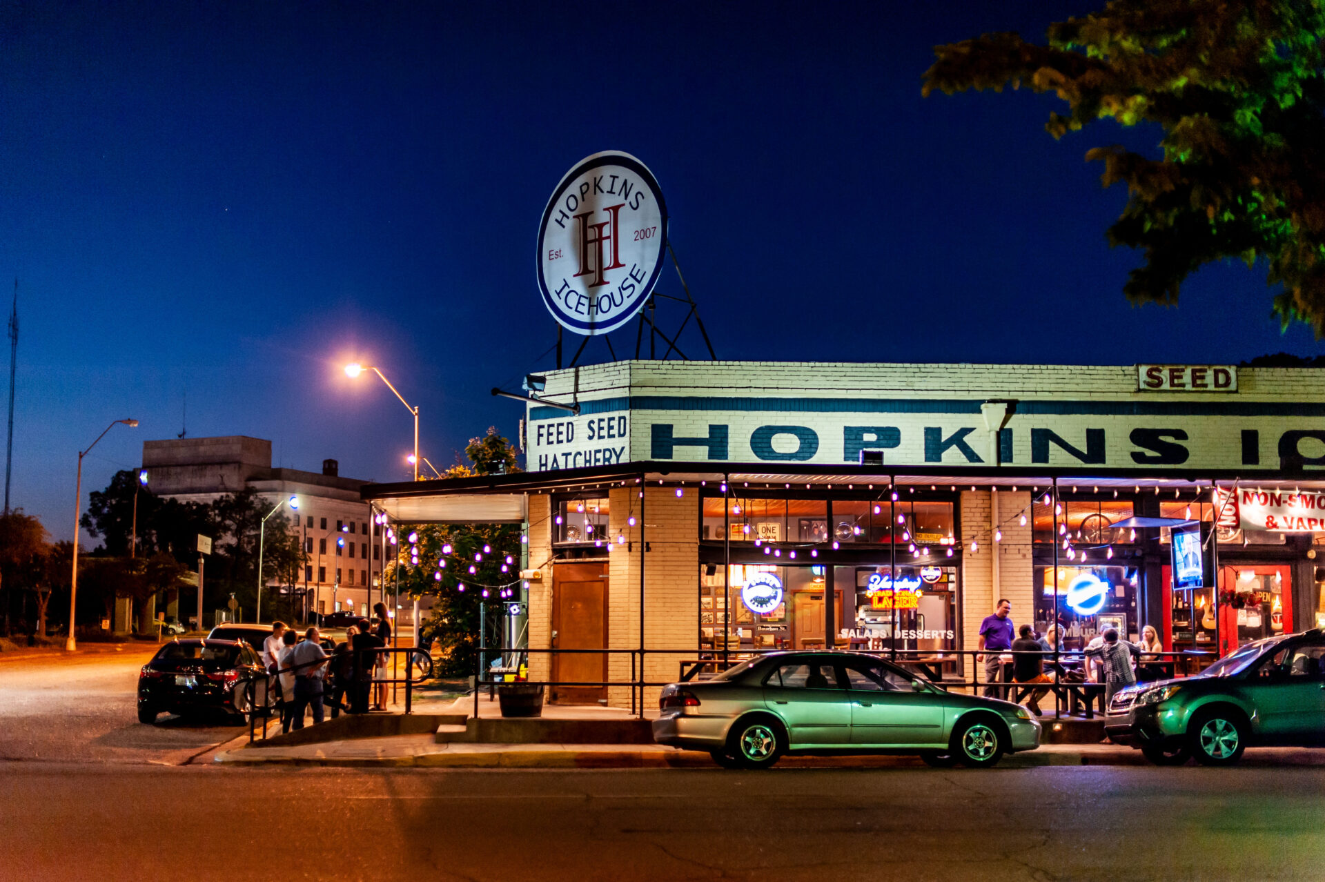 Hopkins Icehouse restaurant in downtown Texarkana, Arkansas, lit up at night with outdoor seating and string lights.