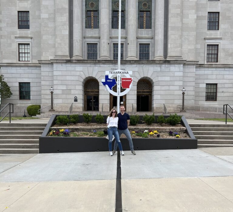 Visitors standing on the Texas–Arkansas state line in front of the Texarkana Post Office and Federal Building.