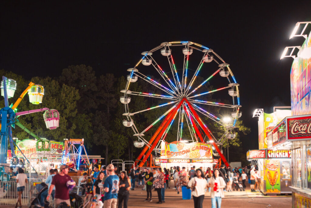 A crowd and brightly lit ferris wheel at night during the Four States Fair in Texarkana, Arkansas