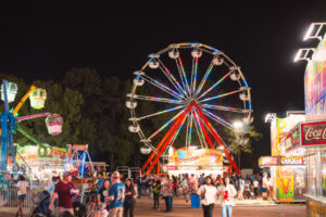 A crowd and brightly lit ferris wheel at night during the Four States Fair in Texarkana, Arkansas