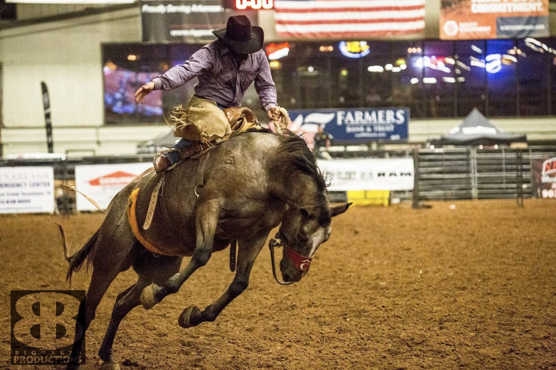 Cowboy riding bucking bull during rodeo event in arena.
