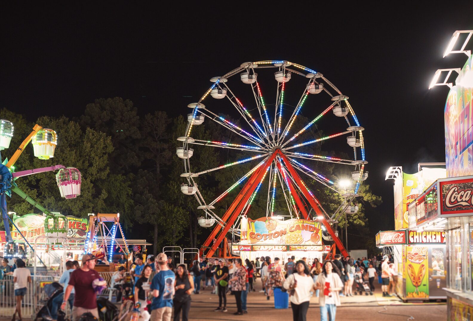 Ferris wheel at Texarkana fair at night with crowd and carnival rides.